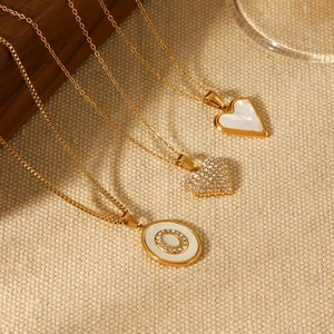 Golden stainless steel heart pendants with shell and crystals on beige textured background