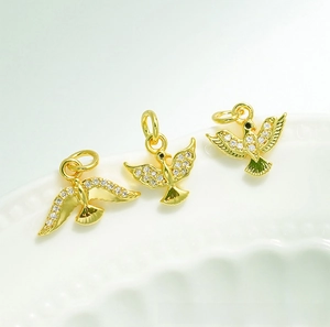 Detailed view of 18K gold-plated bird pendants with white zircon stones on a white plate