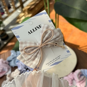 Detail of a brown plaid bow hair clip with an elegant ALLINE brand display card