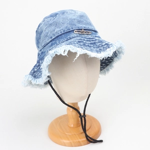 Detail of light blue washed denim bucket hat with frayed edges and metal pin ornament