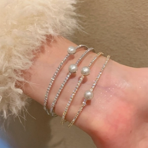 Close-up of stacked gold and silver pearl bracelets with pavé zircons on a wrist