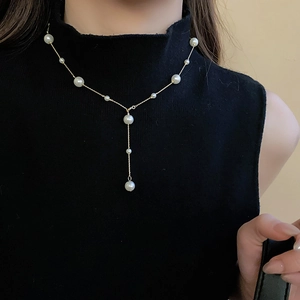 Detailed view of an elegant Y-shaped gold necklace with hanging white pearls on a model