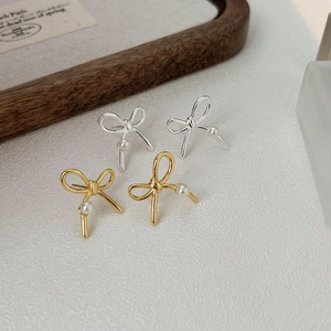925 silver bow-shaped pearl earrings in gold and silver finish on white textured background
