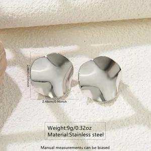 Close-up of wavy irregular silver stainless steel earrings on a stone surface