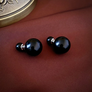 Macro shot of retro black double pearl stud earrings on a dark red satin background