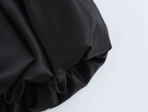 Detailed view of the smooth black satin fabric and pleated texture of the puffy mini skirt