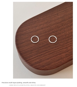 Macro detail of silver hoop earrings showing smooth multi-layer plating on wood stand