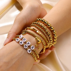 Detail of layered gold beaded bracelets with white LOVE MAMA alphabet beads on silk