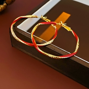 Detail of gold-plated twisted hoop earrings with red enamel finish on leather display
