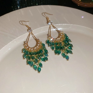 Close-up of gold drop earrings with green crystal tassels and sparkling rhinestones