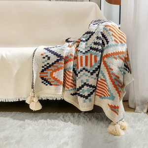 Detail of bohemian knit blanket with geometric patterns and tassels on a beige sofa
