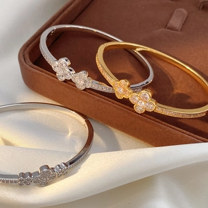 Close-up of zircon-inlaid clover bracelets in silver and gold on a silk surface