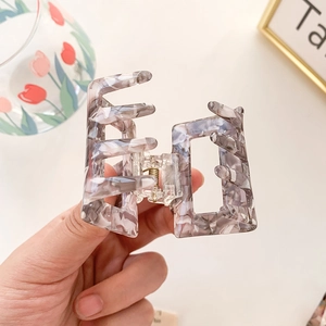 Square acetate shark clip with gray marble texture held by hand for hair styling