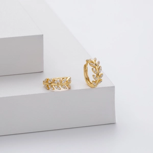 Macro detail of gold leaf-shaped earrings with white zircon on a white display stand