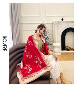 Detail of red faux cashmere scarf with beige floral embroidery in cozy home setting