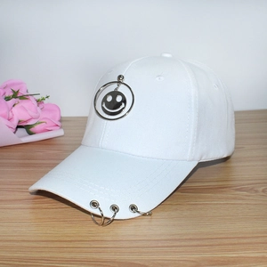 White baseball cap with silver metal rings and smiley face pendant on wooden desk