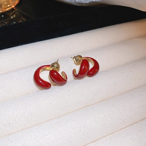 Detail of red and gold C-shaped earrings with high-gloss finish on a jewelry tray