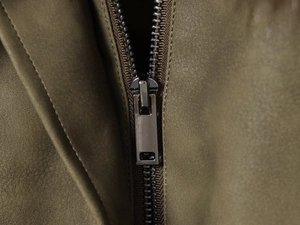 Vue macro d'une fermeture éclair en métal et texture cuir vert olive sur une veste de style français