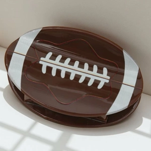 Detail of football-shaped hair claw clip in dark brown acetate with white stitch patterns
