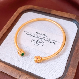 Detail of vintage matte gold cuff featuring green cabochon and red gemstone accents