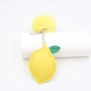 Yellow PU leather lemon keychain with fuzzy pompom on a white display pedestal