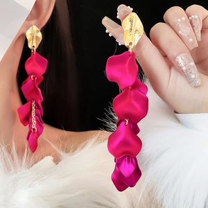 Gros plan de boucles d'oreilles feuilles dorées avec glands de pétales rose rouge sur modèle