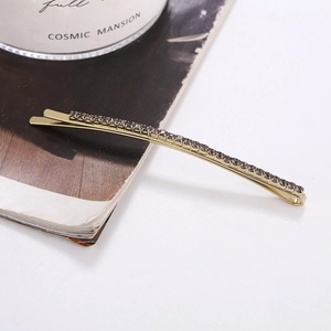 Elegant gold rhinestone hair clip with grey crystals displayed on a stylish desk setup