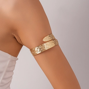 Detailed close-up of golden metal arm cuff with intricate vine pattern and open wrap design