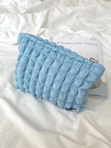 Close-up of light blue quilted bubble textured toiletry bag on white bedsheets