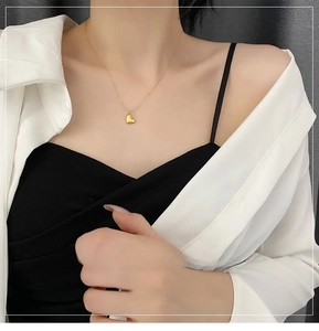 Detailed close-up of a minimalist 18K gold-plated 3D heart necklace on woman's collarbone