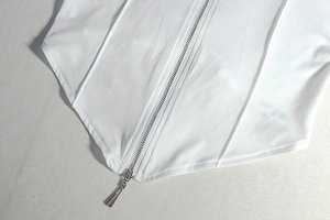 Detail of white corset top featuring metal zipper and asymmetrical triangular hemline