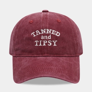 Dettaglio del ricamo bianco TANNED and TIPSY su un cappello in cotone rosso vino lavato