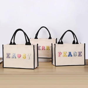 Three stylish canvas tote bags with colorful embroidered letters on a wooden table