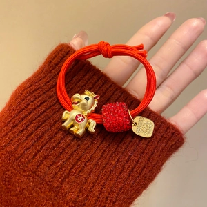 Détail d'un élastique à cheveux rouge avec pendentif cheval doré et breloque porte-bonheur