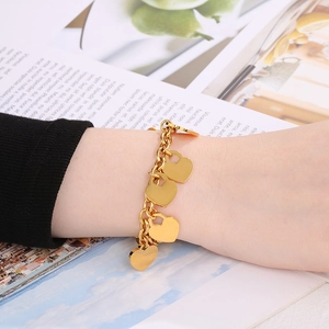 Polished 18K gold heart charms on a chunky chain link bracelet worn on a wrist