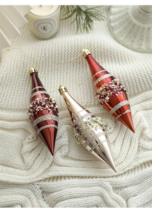 Detailed view of champagne and red beaded spindle Christmas ornaments on knit fabric