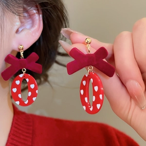 Détail de boucles d'oreilles nœud velours rouge avec pendentif cœurs sur crochets dorés