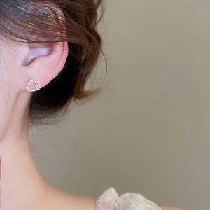 Close-up of a silver cat-shaped stud earring with a pink opal stone worn by a model
