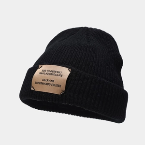 Close-up detail of the black knitted beanie fabric texture and stitched leather patch