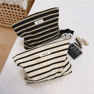 Detail of striped cotton makeup bags in black and beige on a white quilted surface