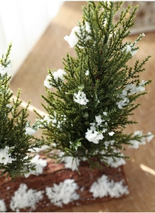 Macro detail of artificial cedar tree showing snowy pine needles and natural wood base