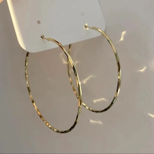 Macro shot of large gold hoop earrings with a textured metallic finish on a white card