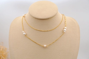 Detail of layered gold chain necklace featuring freshwater pearls and paperclip links