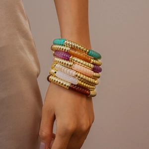 Gros plan d'un ensemble de bracelets superposés en métal doré et perles de résine colorées