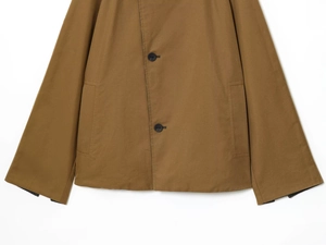 Detail of camel cotton jacket featuring black buttons, side pockets and striped lining