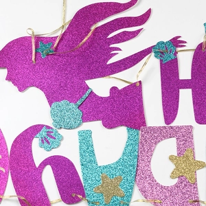Close-up of glittery mermaid banner with purple silhouette and gold starfish decorations