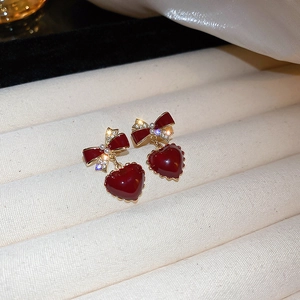 Detail of red heart earrings with golden bow, pearls, and crystals on textured fabric