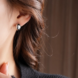Close-up of a silver-plated oval huggie earring on ear for a minimalist jewelry look