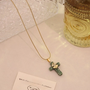 Detail of green natural stone cross pendant with gold bowknot on snake chain necklace