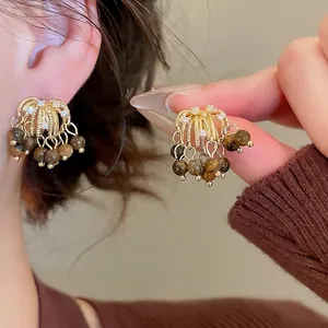 Elegant gold earrings with tiger eye beads and tassels worn by a model in a close-up shot